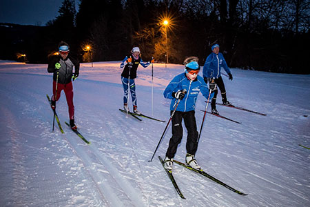 Langläufer am Abend fahren auf der beleuchteten Loipe